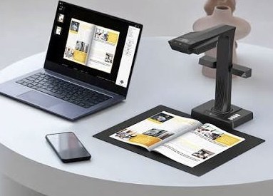 An overhead book scanner on a desk, with the scanned pages appearing on the laptop beside it